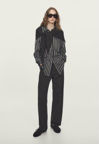 Czarna i biała w paski koszula, czarne spodnie i ciemne okulary przeciwsłoneczne. Czarny sweter zarzucony na ramionach. Gładka faktura, luźny fason.