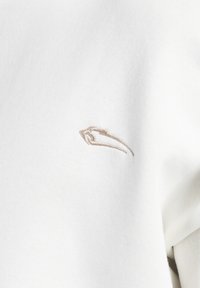 Bílý bavlněný svetr s jemným béžovým vyšitým logem na přední straně. Jednoduchá, měkká textura s klasickým designem.