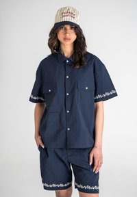 Marineblå sæt med kortærmet skjorte og shorts med striber, prydet med blomstermønstrede kanter på ærmerne og kanten, knaplukning foran og brystlommer.