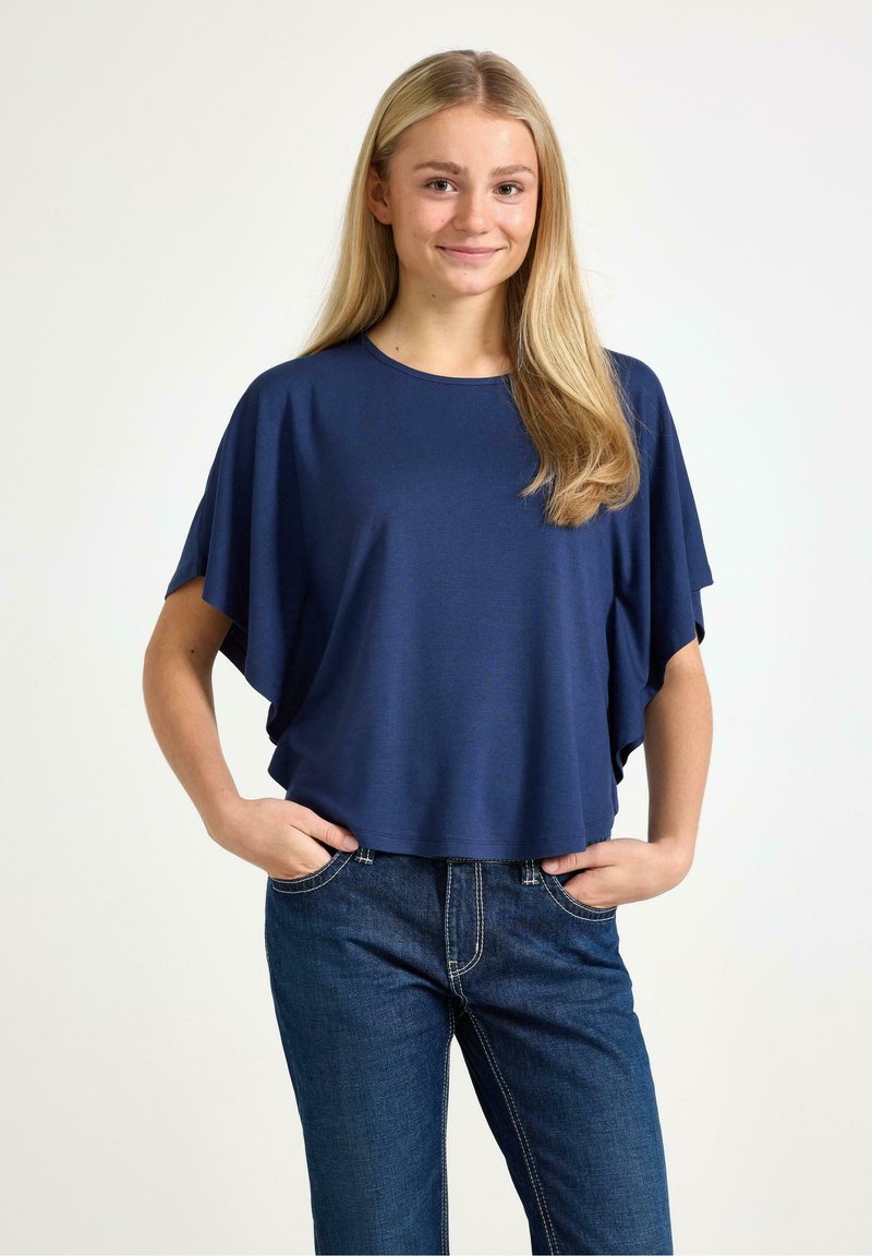 Mörkblå, kortärmad topp med en ledig, boxig passform och en rund halsringning. Bärs med blå denimjeans, som har fickor och kontrastsömmar.