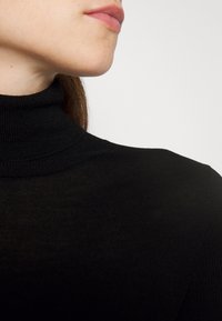 Haut en tricot noir à col roulé avec une texture côtelée ajustée. Gros plan mettant en avant le col montant et le tissu lisse.