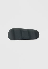 Μαύρη ελαστική σόλα παπουτσιού με οριζόντιες αυλακώσεις, στρογγυλή μύτη και ανάγλυφο λογότυπο στο κέντρο. Λείο υλικό με ανθεκτική επιφάνεια.