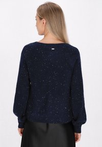 Dunkelblauer gestrickter Pullover mit texturierter Oberfläche, der einen lässigen Schnitt und lange Ärmel hat, sowie einem subtilen metallischen Akzent auf der Rückseite.