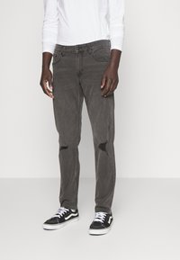 Grå denimjeans med slitte kne detaljer, en klassisk passform, og lommer, i kombinasjon med svarte og hvite sneakers.