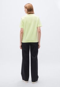 Ανοιχτό πράσινο κοντομάνικο μπλουζάκι με άνετη εφαρμογή, συνδυασμένο με σκούρα παντελόνια με φαρδιά μπατζάκια και ανοιχτόχρωμα παπούτσια, με θέα από πίσω.