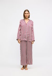 Pajama set z navpičastim vzorcem v maroon in krem barvi, ki vključuje srajco na gumbe z dolgimi rokavi in široke hlače, izdelane iz mehkega blaga.