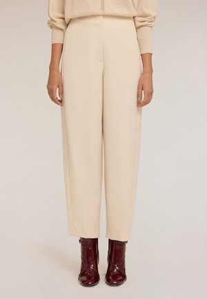 Pantalones de pierna ancha color beige con una tela suave y cintura alta. Cuentan con bolsillos laterales y se combinan con botas de tobillo burdeos brillantes.