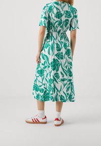 Robe midi à motifs floraux verts avec une taille élastique, des manches courtes, portée avec des baskets blanches avec des accents rouges.