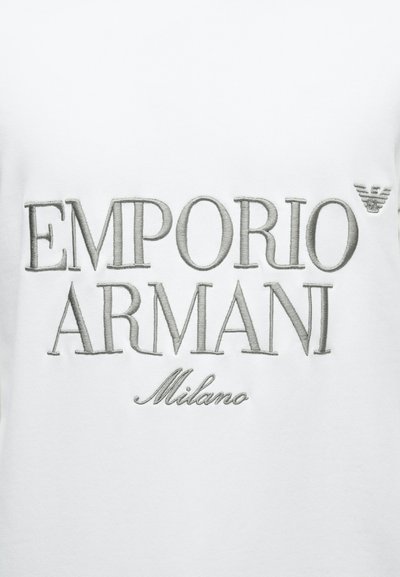 Sweatshirt branca com texto bordado "EMPORIO ARMANI Milano" em cinza-prateado, com um logótipo subtil no canto superior direito.