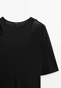 Top nero a coste con maniche corte e aperture sulle spalle. Presenta un collo a giro e tessuto testurizzato. Etichetta visibile all'interno.