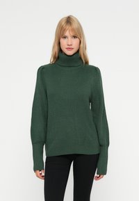 Suéter verde malhado com gola alta, mangas largas e textura canelada. Apresenta um corte relaxado e discretos detalhes nos ombros.