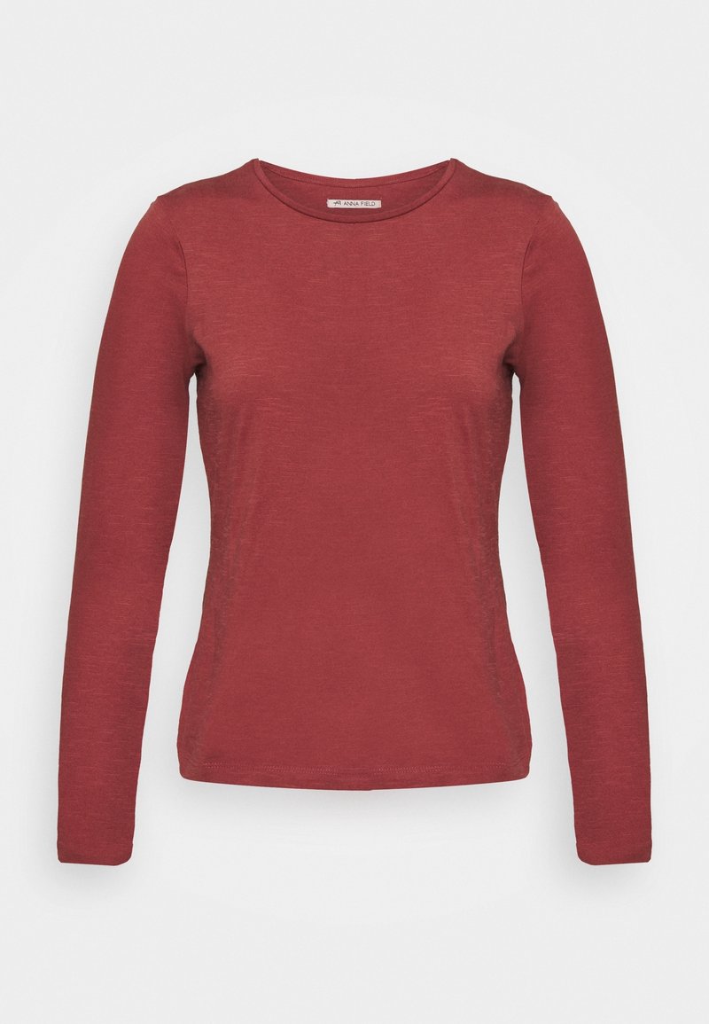 T-shirt rouge à manches longues en tissu léger et lisse, avec un col rond et une silhouette ajustée. Design simple, sans motifs ni accents.