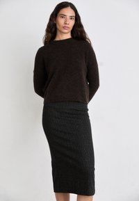 Dunkelbrauner, fuzzy Strickpullover mit Rundhalsausschnitt, kombiniert mit einem figurbetonten, schwarz-weißen gestreiften Bleistiftrock. Strukturiertes Material bei beiden Teilen.