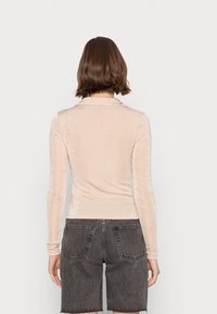 Långärmad, ljusbeige topp i mjukt, sammetsliknande tyg. Har en klassisk krage och en figursydd design, ihop med grå shorts.