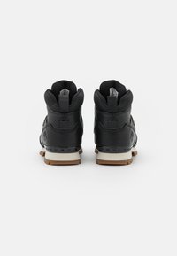 Pár černých vysokých tenisek Timberland z pohledu zezadu, s polstrovanými límci a hnědými gumovými podrážkami na bílém pozadí.