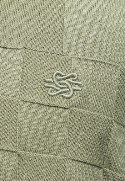 Πλεκτό ύφασμα πατσγουόρκ σε απαλό πράσινο με κεντητό αφηρημένο σχέδιο κόμπου στο κέντρο.