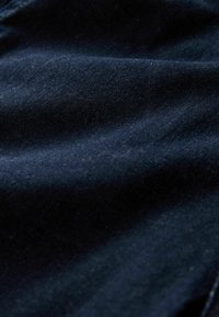 Nahaufnahme von dunkelblauem Denimstoff, der Textur und subtile Falten in sanftem Licht zeigt.