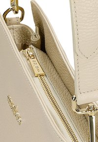 Interno di borsa a tracolla in pelle beige con chiusura a zip dorata, che mostra un materiale testurizzato e un compartimento con una tasca piccola.