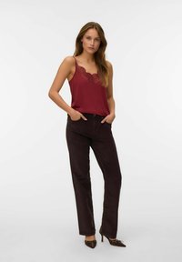 Burgunderfarvet camisole med blonderførelse, parret med mørkebrune fløjlsbukser, der har en tætsiddende pasform og en glat tekstur. Højhælede sko fuldender looket.