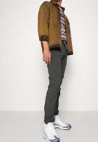 Brun, urtvättad denimjacka över en randig t-shirt, matchad med mörkgröna byxor och grå sneakers med neonlysande detaljer. Avslappnad outfit.