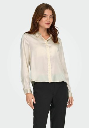 Zijdecrème blouse met een kraag, knoopsluiting aan de voorkant en lange mouwen. Het heeft een rechte zoom en een gladde, glanzende textuur.