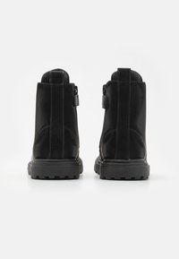 Botas negras de tobillo con acabado de ante, que presentan un tacón texturizado, cremallera lateral y suela de goma resistente con patrones de agarre.