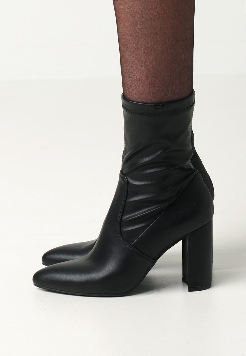 Černé kožené kotníkové boty se sklápěním, špičatou špičkou a robustním podpätkem. Hladká textura s jemným šitím a bez viditelného kovového kování.