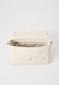Bolso sintético de color crema, de textura suave, con apertura con cremallera, herrajes en plata y un diseño minimalista. El interior incluye un pequeño bolsillo.