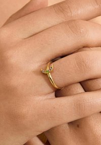 Anillo de oro con un diseño de media luna, decorado con pequeñas piedras preciosas coloridas. Textura suave con un acabado pulido, apoyado en una mano.