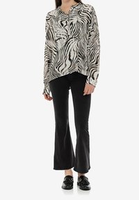 Czarno-biała bluzka w print zebry z dekoltem w serek i długimi rękawami, zestawiona z czarnymi dzwonami i czarnymi loafersami.