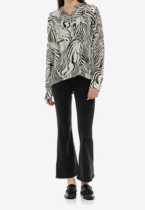 Schwarz-weiße Zebra-Print-Bluse mit V-Ausschnitt und langen Ärmeln, kombiniert mit schwarzen Schlagjeans und schwarzen Loafers.
