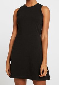 Robe noire sans manches en coton doux. Elle dispose d'un col rond et d'une coupe décontractée, sans motifs ni accents visibles.