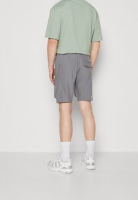 Šedé cargo šortky s elastickým pasem a boční kapsou, spárované se světlezeleným tričkem s kulatým výstřihem a bílými sportovními botami.