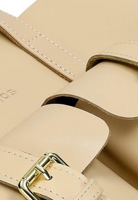 Beige leren tas met twee gebogen handvatten en een gouden metalen gesp. Opvallende stiksels langs de randen. Zachte textuur.
