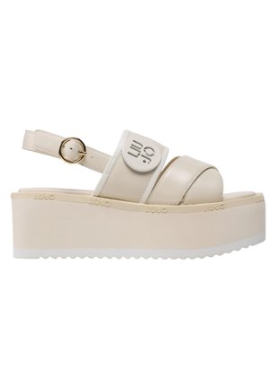Sandali platform beige con cinturino largo, cinturino alla caviglia regolabile e dettaglio con logo circolare. Suola testurizzata con bordi seghettati.