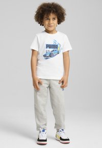 Camiseta blanca de algodón con un gráfico de un coche azul y el texto "PUMA", combinada con pantalones de chándal grises y zapatillas negras con acentos amarillos.
