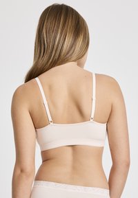 Ljusrosa bralette med justerbara band, slät textur och en bred banddesign. Har delikata spetsdetaljer längs fållen.