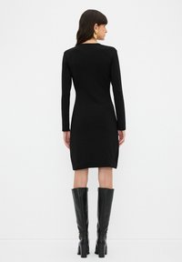 Schwarzes, langärmliges Bodycon-Kleid mit Rundhalsausschnitt, knielangem Saum und glatter Textur, kombiniert mit knielangen schwarzen Stiefeln.