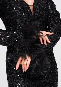 Robe noire en sequins avec un décolleté plongeant en V et des manches longues ornées de plumes noires. Gros plan sur les détails des mains et la texture.