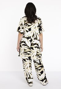 Schwarzes und weißes Blumenoutfit mit einem lockeren kurzärmeligen Oberteil und passenden weit geschnittenen Hosen mit gelben Akzenten. Glattes, leichtes Material.
