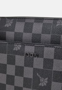 Borsa in pelle a quadretti nera con superficie texturizzata, caratterizzata da sottili motivi floreali e un logo metallico "JOOP!" sul davanti.