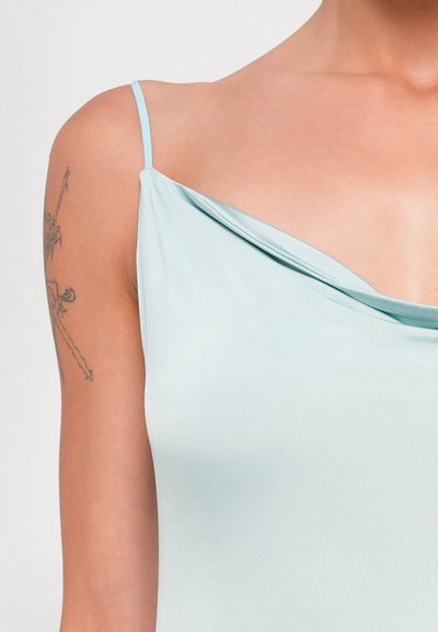 Lichtblauwe camisole met een gedrapeerde halslijn en dunne bandjes, gemaakt van gladde stof. Close-up weergave benadrukt schouder- en armbereik.