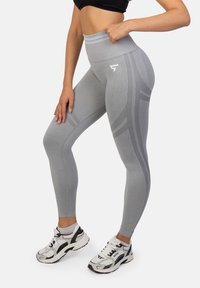 Szare legginsy o wysokim stanie z teksturowanym wzorem i odblaskowymi akcentami, połączone z czarno-białymi butami sportowymi.