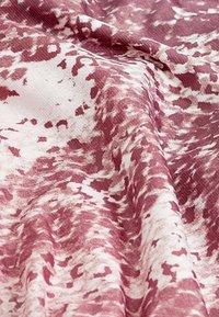 Tessuto testurizzato in tonalità di bordeaux e crema, con un motivo astratto che fonde i colori in un design fluido.