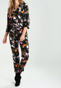Ensemble de pyjama à motifs avec un fond noir et des motifs floraux colorés en rose, orange et vert. La matière est légère avec une coupe décontractée.