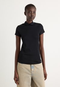 Zwarte polo met korte mouwen, een kraag en een slim fit; gemaakt van zachte stof met minimale details aan de zoom. Draagt met lichte jeans.