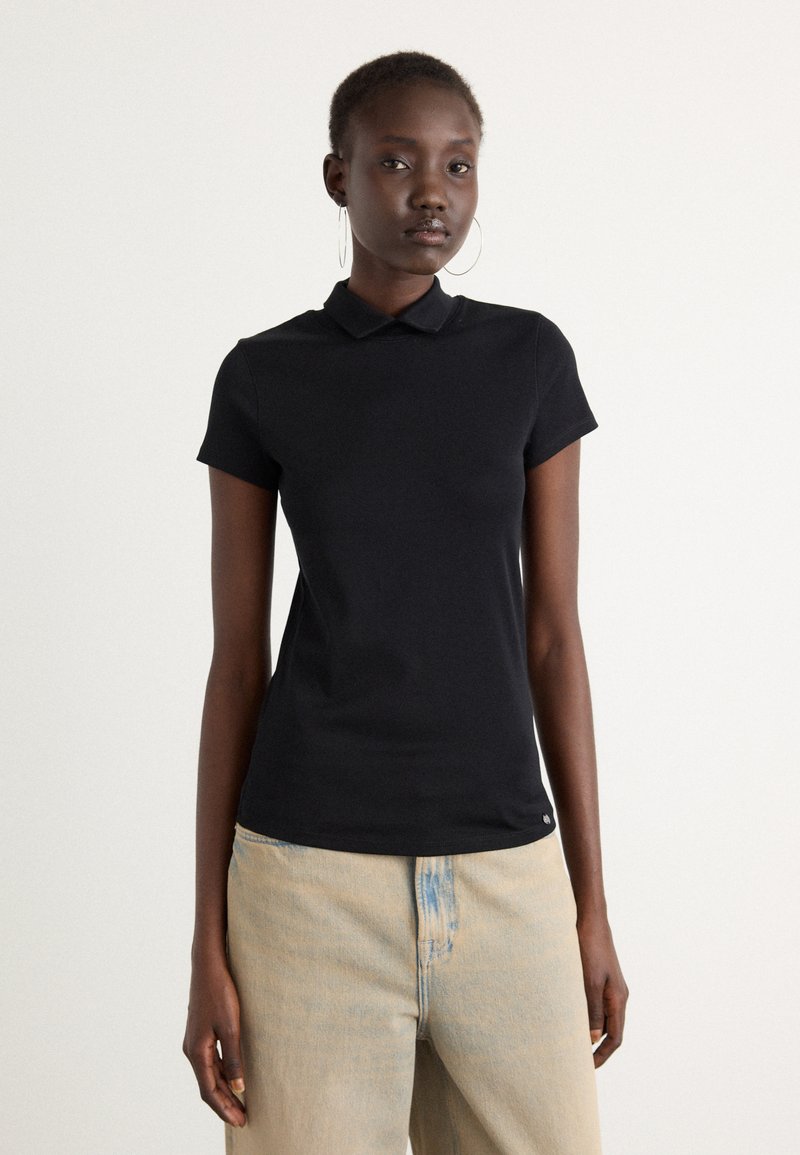 Zwarte polo met korte mouwen, een kraag en een slim fit; gemaakt van zachte stof met minimale details aan de zoom. Draagt met lichte jeans.