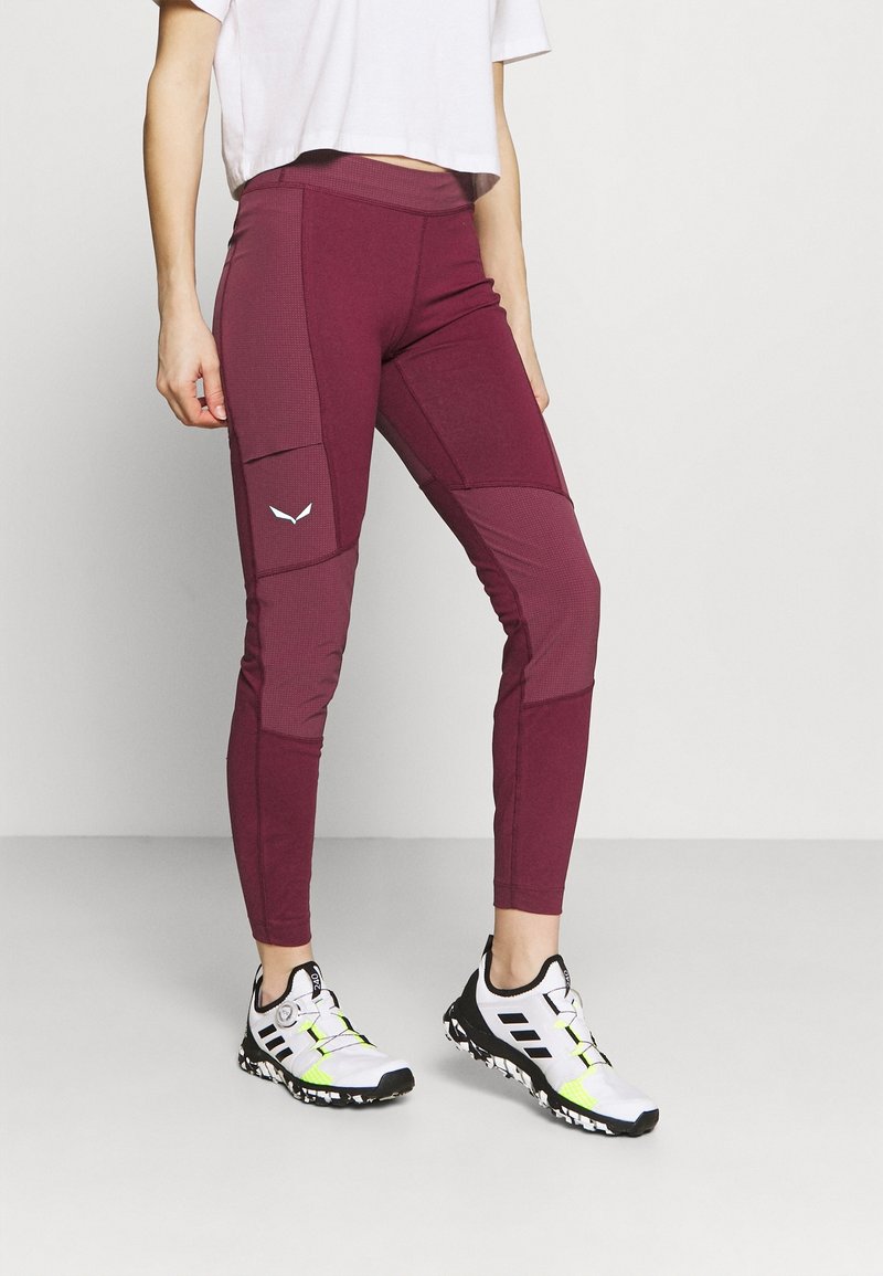 Burgundy leggings med en figurnära design, texturerade detaljer och sidofickor. Kombinerade med vita sportskor med gula detaljer.