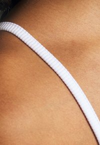 Sangle blanche à ribans sur une peau brune, mettant en valeur la texture lisse de la peau et le motif régulier de la sangle. Accent sur les détails de la sangle.