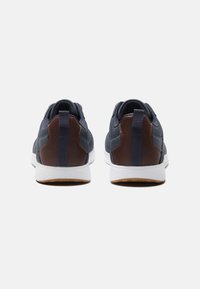 Navy athletic sneakers with a brown leather accent, white midsole, and textured upper. Features a pull tab at the heel for easy wear.